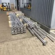 Gestapelte Metallrohre vor Industriehalle, bereit zur weiteren Verarbeitung.